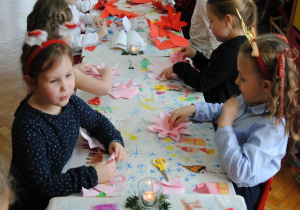 przy stolikach dzieci składają z kolorowego papieru gwiazdy betlejemskie